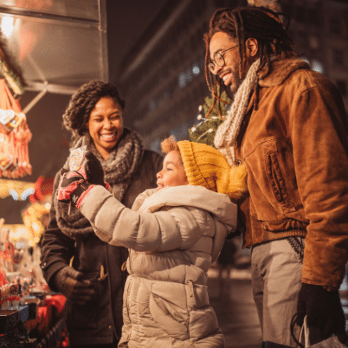 Photo of a family stopped so the child in front can take a photo of a store display of ornaments. They are all wearing winter coats.