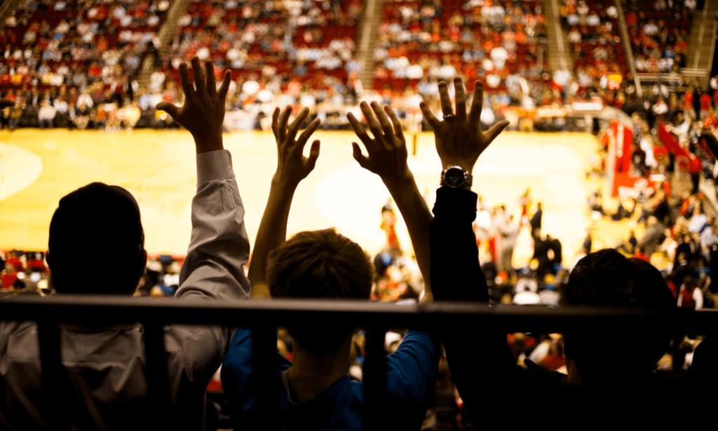 View of people sitting on bleachers with their hands in the air at a basketball game