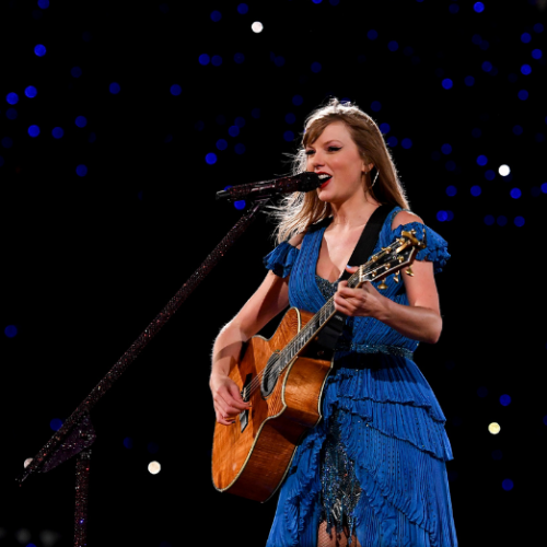 Photo of Taylor Swift in a blue dress with a guitar singing on stage.